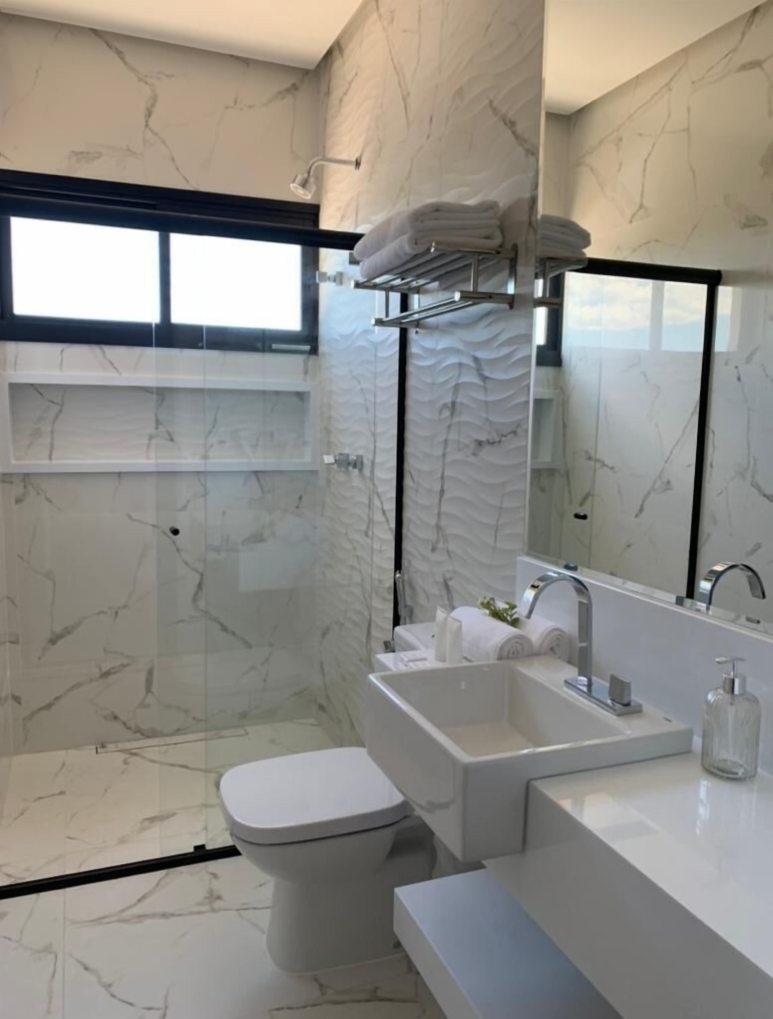Un baño moderno con piso de mármol, cabina de ducha de vidrio, inodoro blanco y lavamanos con espejo.