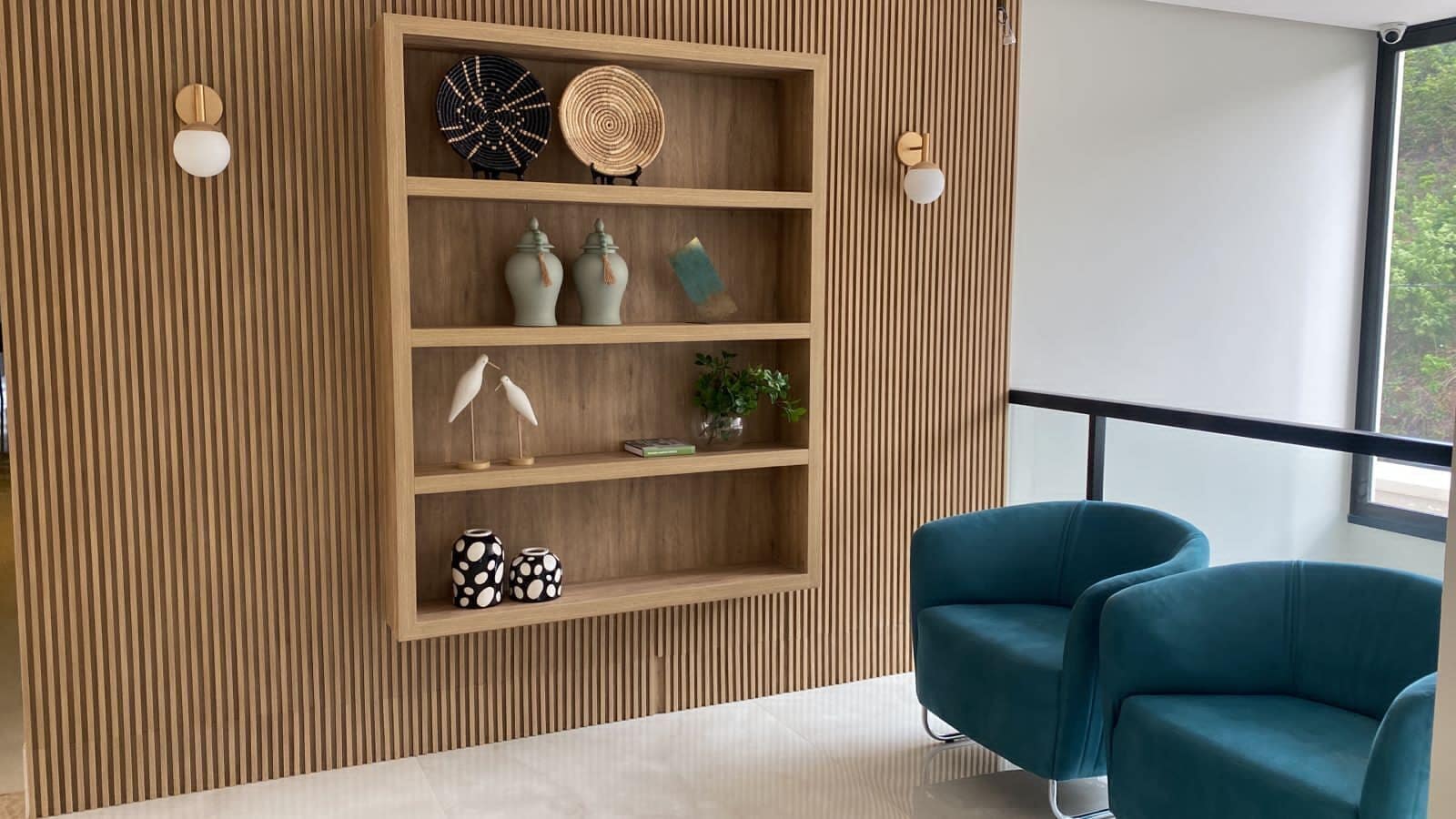 A modern interior with a wooden slatted wall, a blue armchair, and a shelf with decorative items.