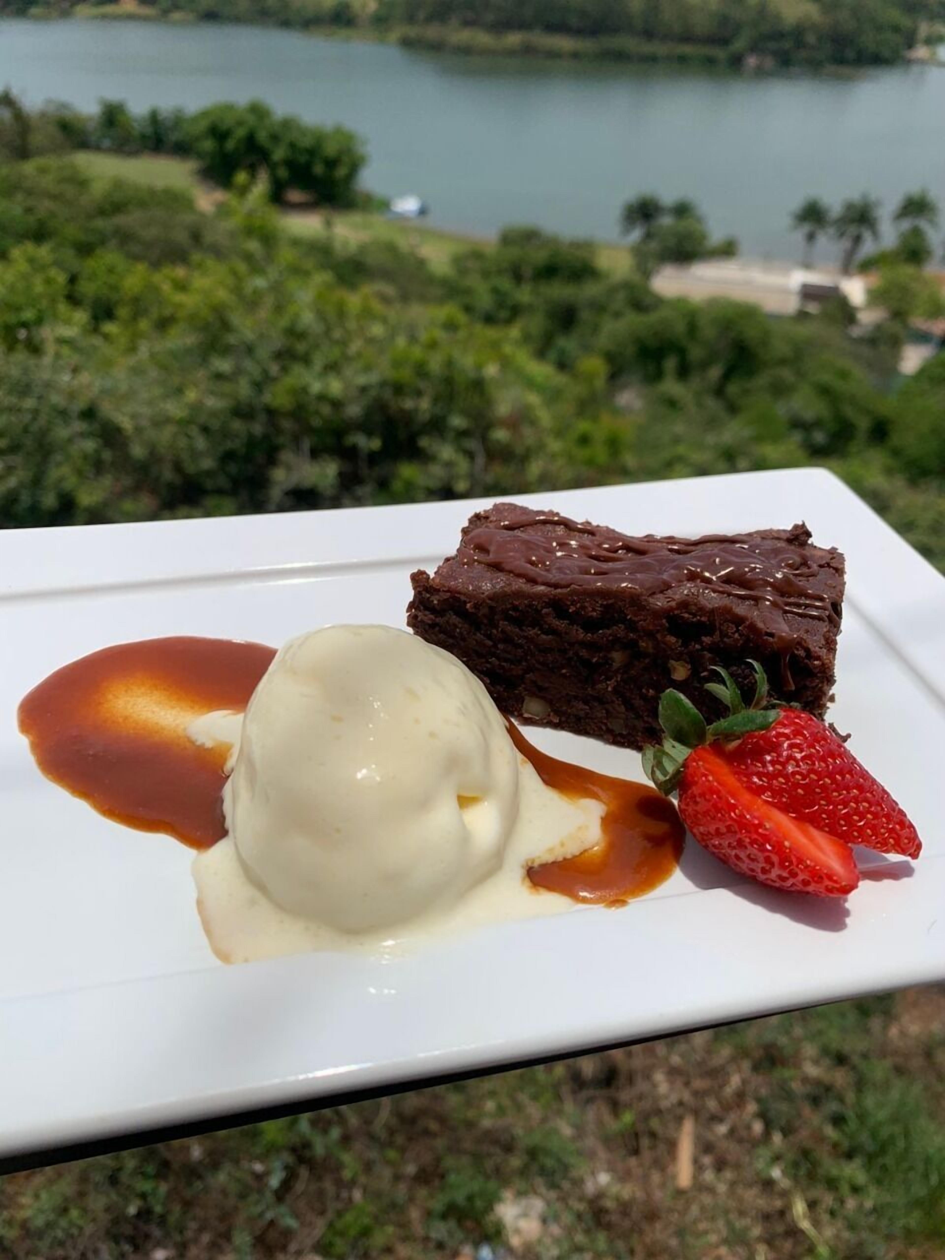 Un plato de postre con un brownie, helado y una fresa sobre un plato blanco.