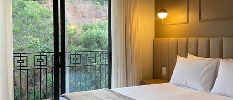 Una habitación de hotel con una cama grande, un balcón con vistas a zonas verdes y un equipo de aire acondicionado.