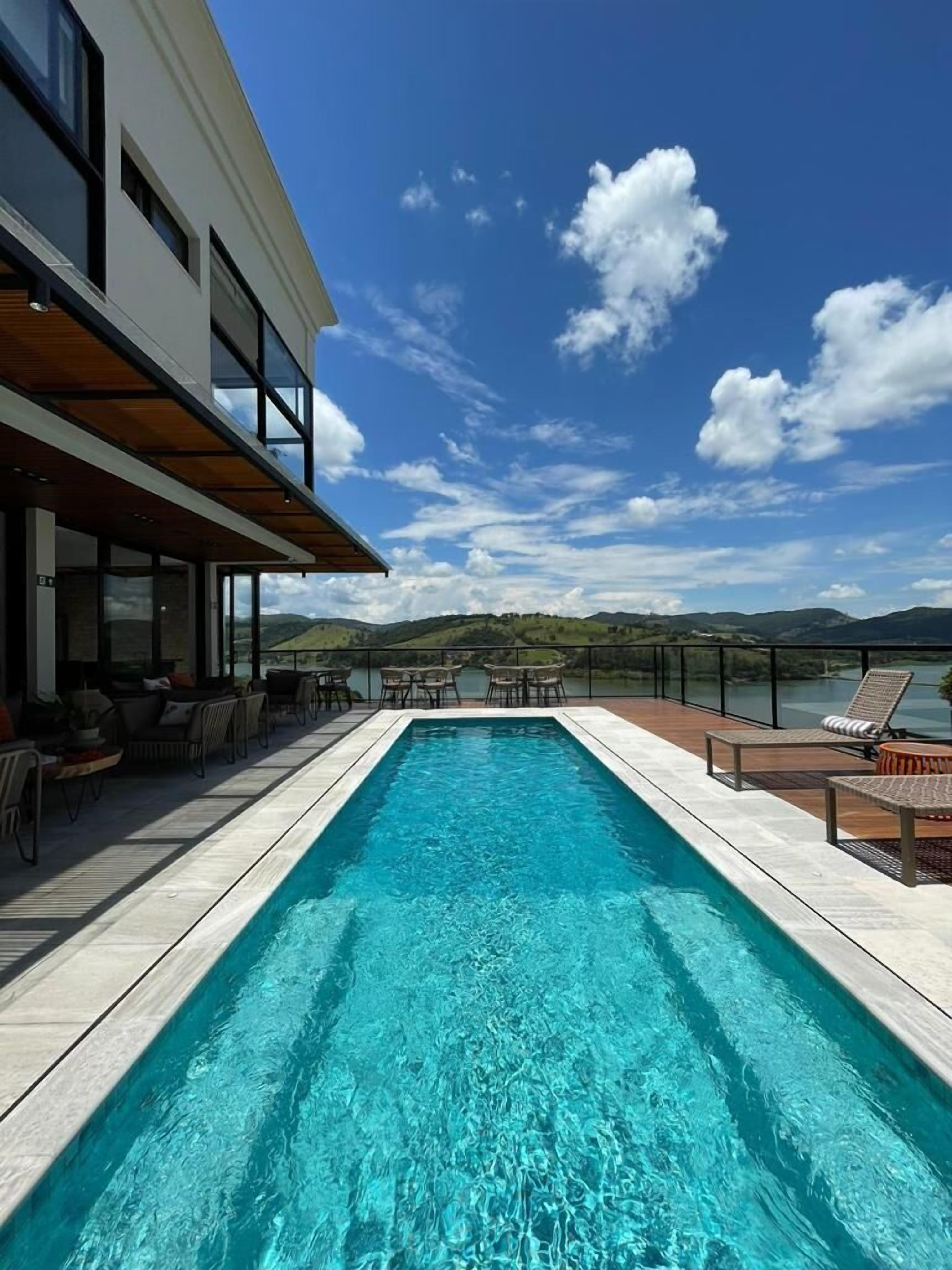 A rectangular swimming pool with clear blue water, surrounded by wooden deck and outdoor furniture.
