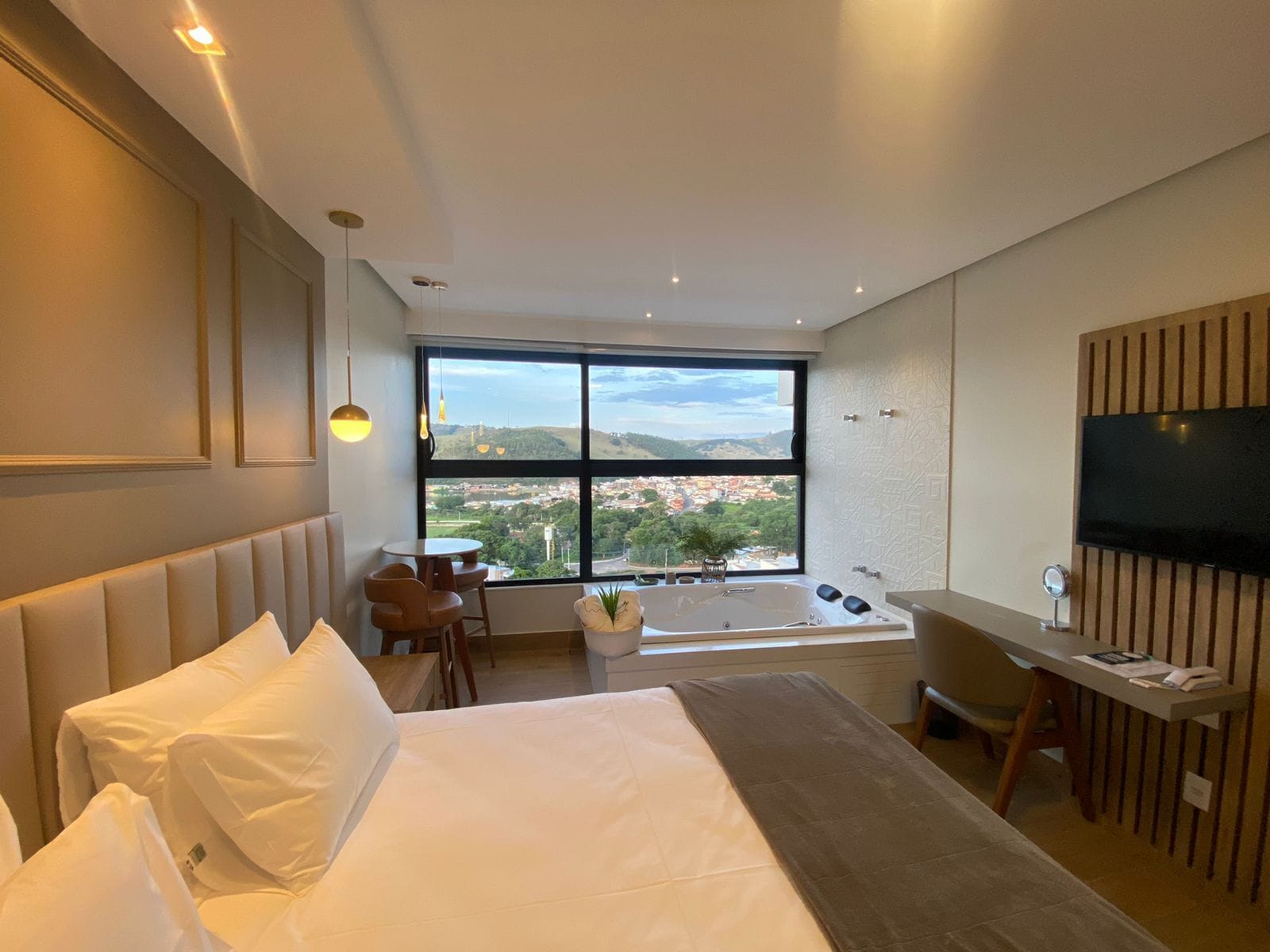 A modern hotel room with a large bed, a desk, a chair, a bathtub, and a TV.