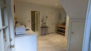 A hallway with a white refrigerator, a small table with a tray, and a wooden shelf unit with kitchen items. - Private two story guesthouse in Takoma Park (Takoma Park)