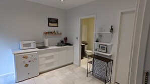A compact kitchen with a microwave, sink, and refrigerator. There are shelves above the counter holding various items. - Private two story guesthouse in Takoma Park (Takoma Park)