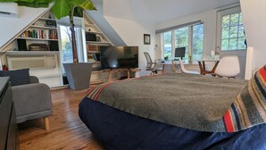 A bedroom with a large bed, a TV, a desk with a computer, a bookshelf, and a window. - Private two story guesthouse in Takoma Park (Takoma Park)