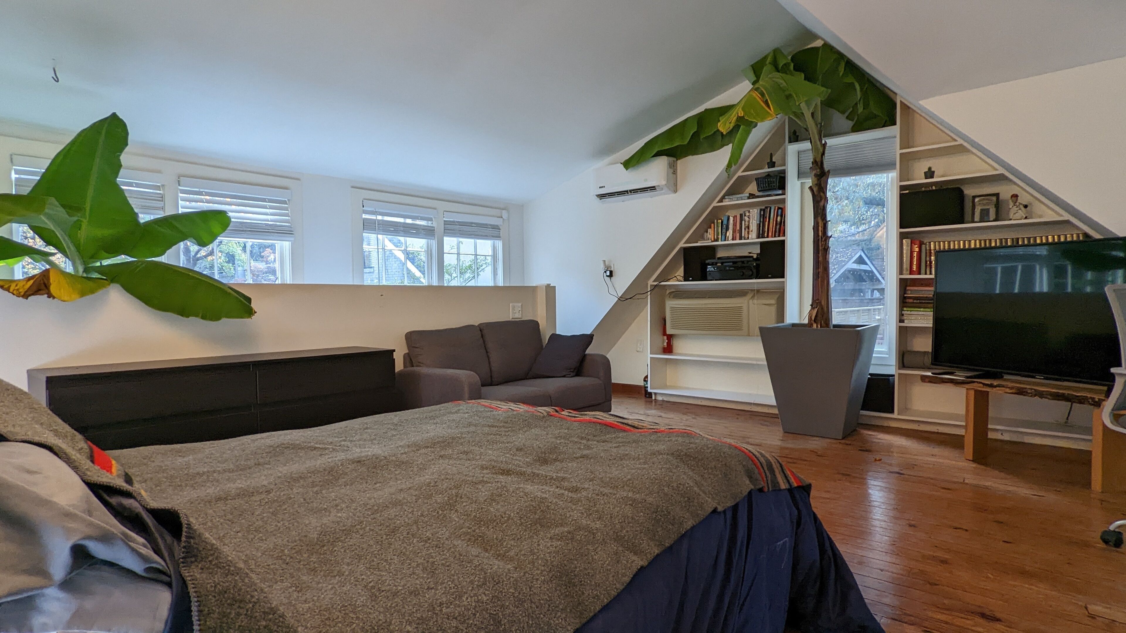 A modern loft bedroom with a large bed, a sofa, a TV, and a bookshelf.