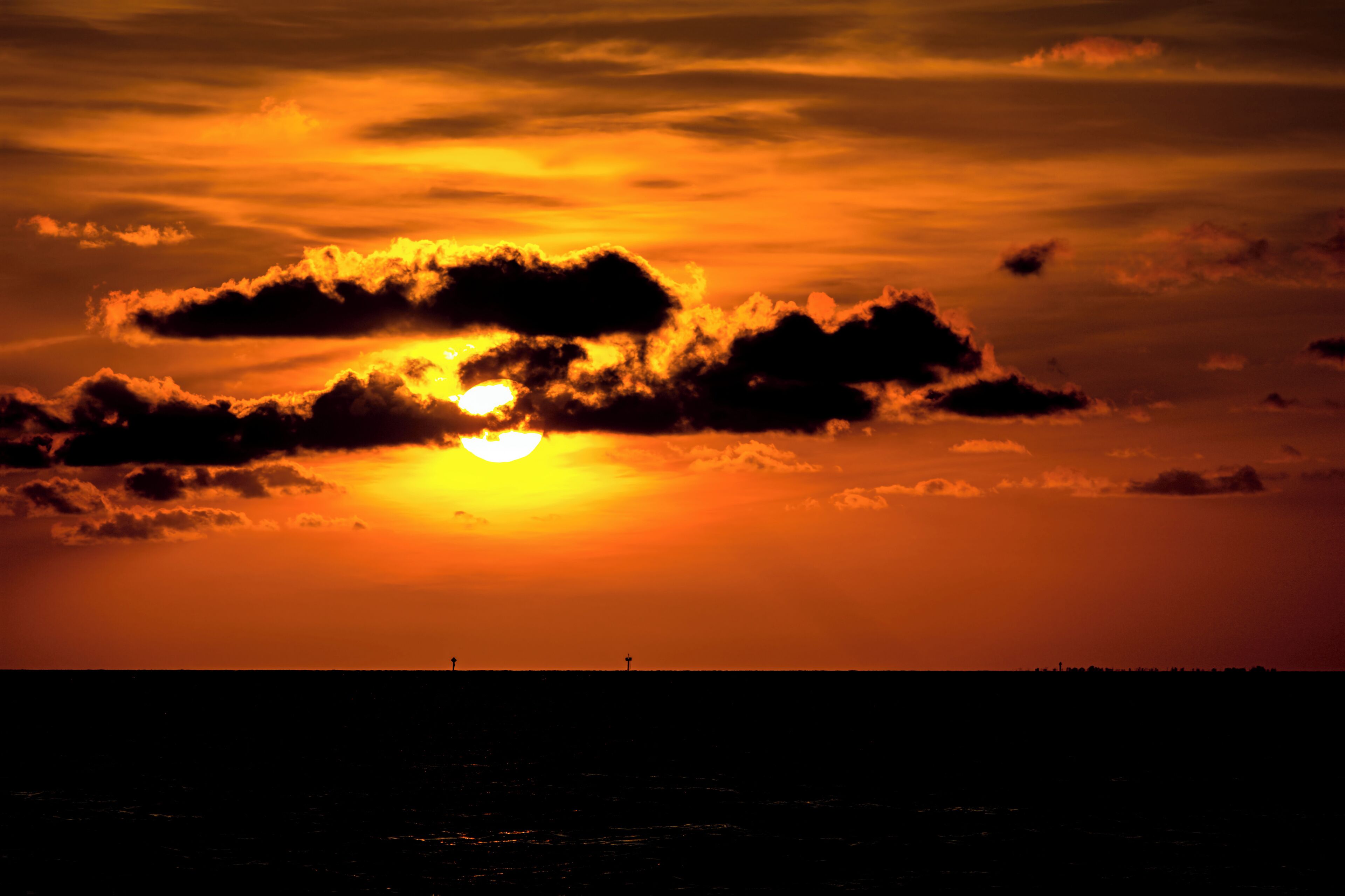 Un coucher de soleil sur une étendue d’eau, avec les silhouettes de bâtiments qui se dessinent à l’horizon.
