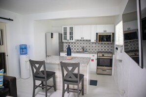 A compact kitchen with white cabinets, a granite countertop, a water dispenser, and a built-in oven.