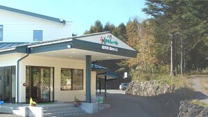 Un edificio con un vestíbulo cubierto, un letrero con caracteres japoneses y un estacionamiento con muro de piedra y bancos.