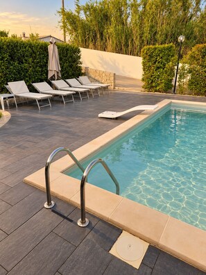 A swimming pool with a clear blue water, surrounded by lounge chairs and a stone wall. - MarinaBlue Haven (Santa Maria del Focallo)
