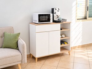 Un mobile bianco con forno a microonde e macchina del caffè sopra, un divano con un cuscino verde e una finestra con persiane.