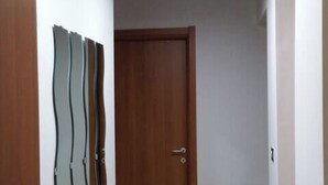A hallway with a wooden door, a wall-mounted mirror, and a tiled floor.