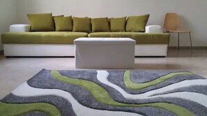 A modern living room with a white sofa, green cushions, a white ottoman, and a patterned rug. - Villa with Pool and Whirlpool (Santa Maria del Focallo)