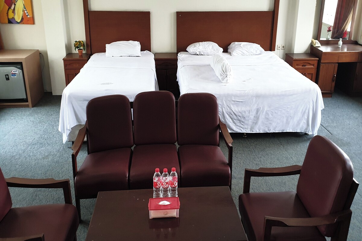 Une chambre d’hôtel avec deux lits, un petit bureau, une chaise et une table sur laquelle se trouve un présentoir pour bouteilles d’eau.