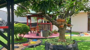 Un espace jardin agrémenté d’un kiosque en bois, d’un petit arbre et de plantes en pot.