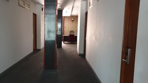 A hallway with a carpeted floor, a wooden door on the right, and a red chair in the distance. - WIR Hotel by Zuzu (Lembongan Island)