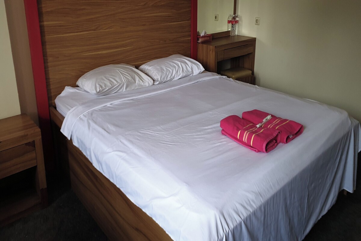Un lit bien fait, avec du linge de lit blanc et une serviette rose posée sur le pied de lit.