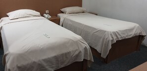 Deux lits simples avec du linge de lit blanc, un téléphone sur la table de chevet et une tête de lit en bois.
