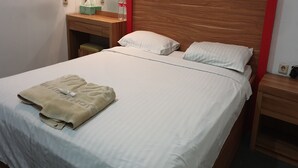A neatly made bed with a folded towel and a bottle of water on the nightstand. - WIR Hotel by Zuzu (Lembongan Island)