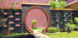 Un arc en briques mène à un bâtiment dont le mur est de couleur rouge et présente une texture particulière, et dont le toit est recouvert de tuiles.