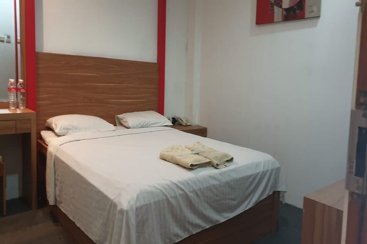 Una cama bien hecha con cabecera de madera, una mesita de noche con lámpara y una obra de arte colgada en la pared.