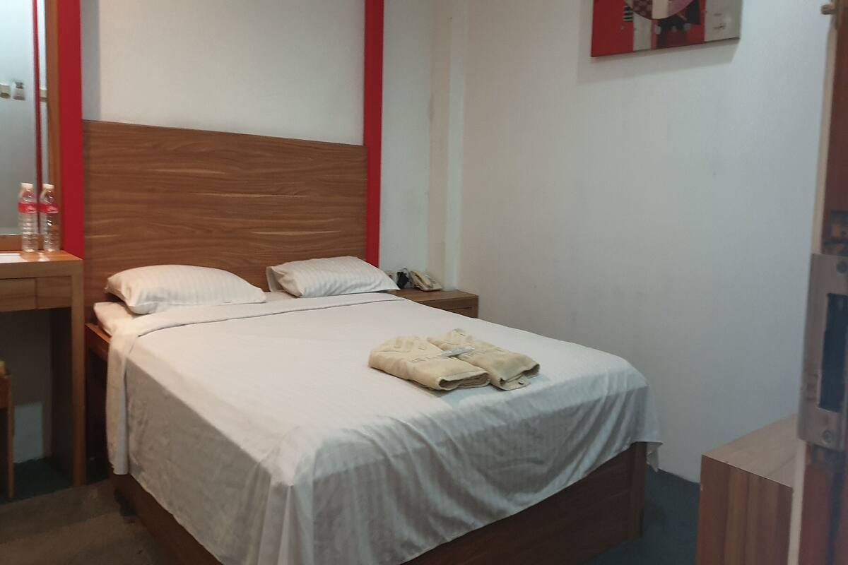 A neatly made bed with a wooden headboard, a bedside table with a lamp, and a wall-mounted artwork.