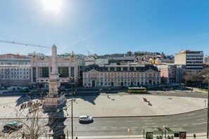 Ein weitläufiger Stadtplatz mit einem markanten Denkmal, einer Straßenbahnlinie und einer Mischung aus historischen und modernen Gebäuden.