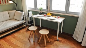 A compact room with a sofa, a small table with a plant, a bowl of fruit, and a window with a view. - Mojito Breeze in Lisbon by Misha s Place 3C (Lisbon)