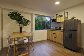 A modern kitchen with wooden cabinets, a stainless steel refrigerator, a dining table with chairs, and a large window overlooking greenery. - #4 Provenza Oasis - Quiet 1BR (Medellín)