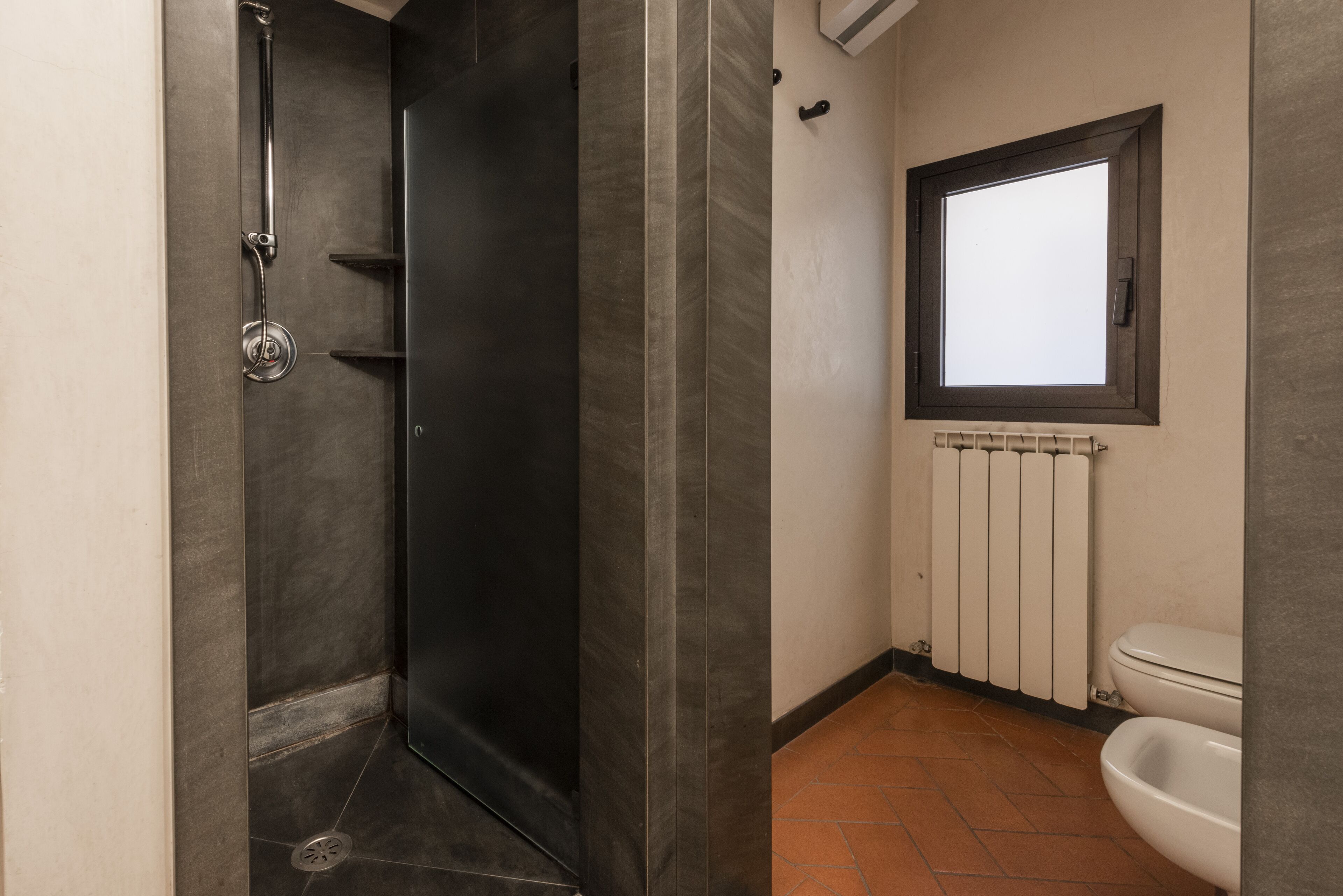 A bathroom with a shower, toilet, and a window.