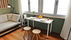 Um espaço de estar compacto com sofá, uma mesinha com comida e bebidas, e uma janela com vista.