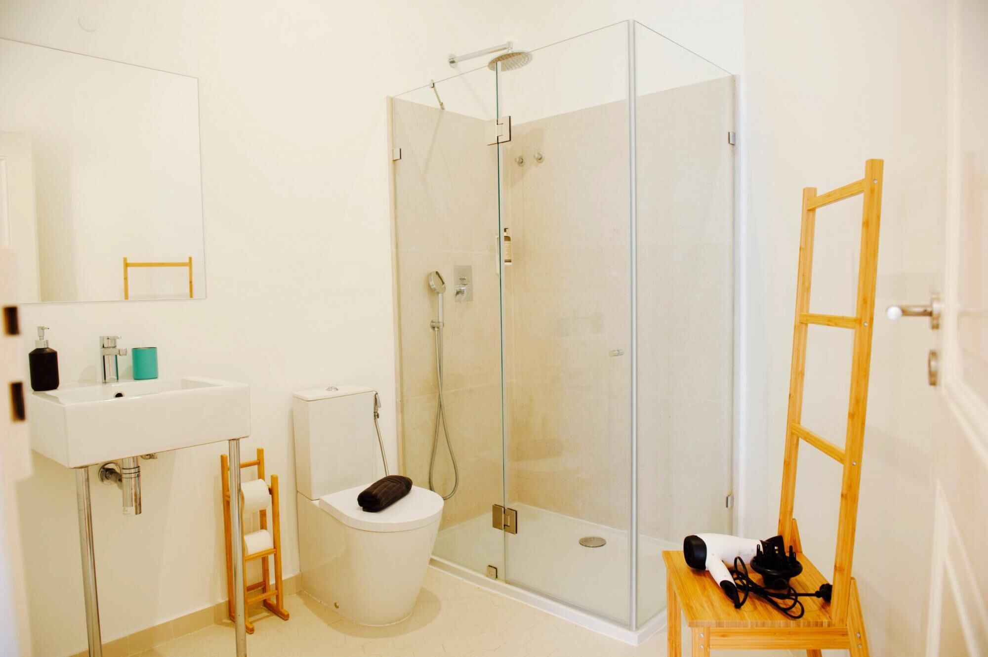 Un baño moderno con ducha de vidrio, lavamanos blanco, inodoro y una silla de madera.