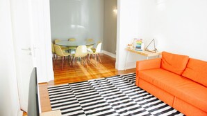 A modern living room with a glass dining table, yellow chairs, a black and white striped rug, and an orange sofa. - Beautiful Dreamers Avenida Liberdade Cr3d (Lisbon)