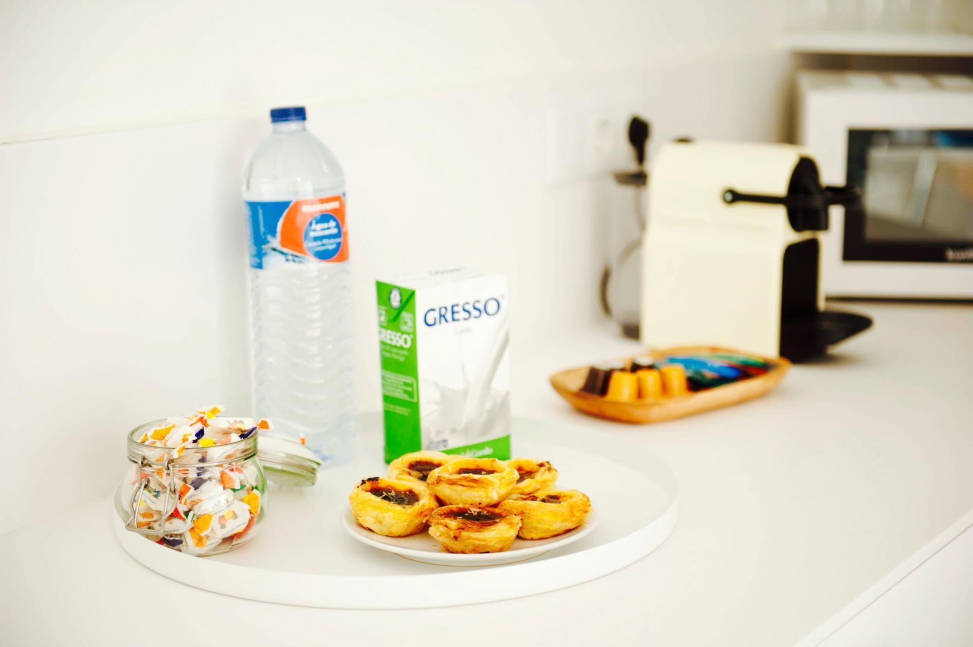 A kitchen counter with a plate of pastries, a jar of colorful candies, a bottle of water, a carton of milk, and a box of coffee creamer.