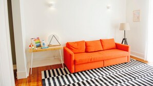 A bright room with a wooden desk, a bright orange sofa, and a black and white striped rug. - Beautiful Dreamers Avenida Liberdade Cr3d (Lisbon)