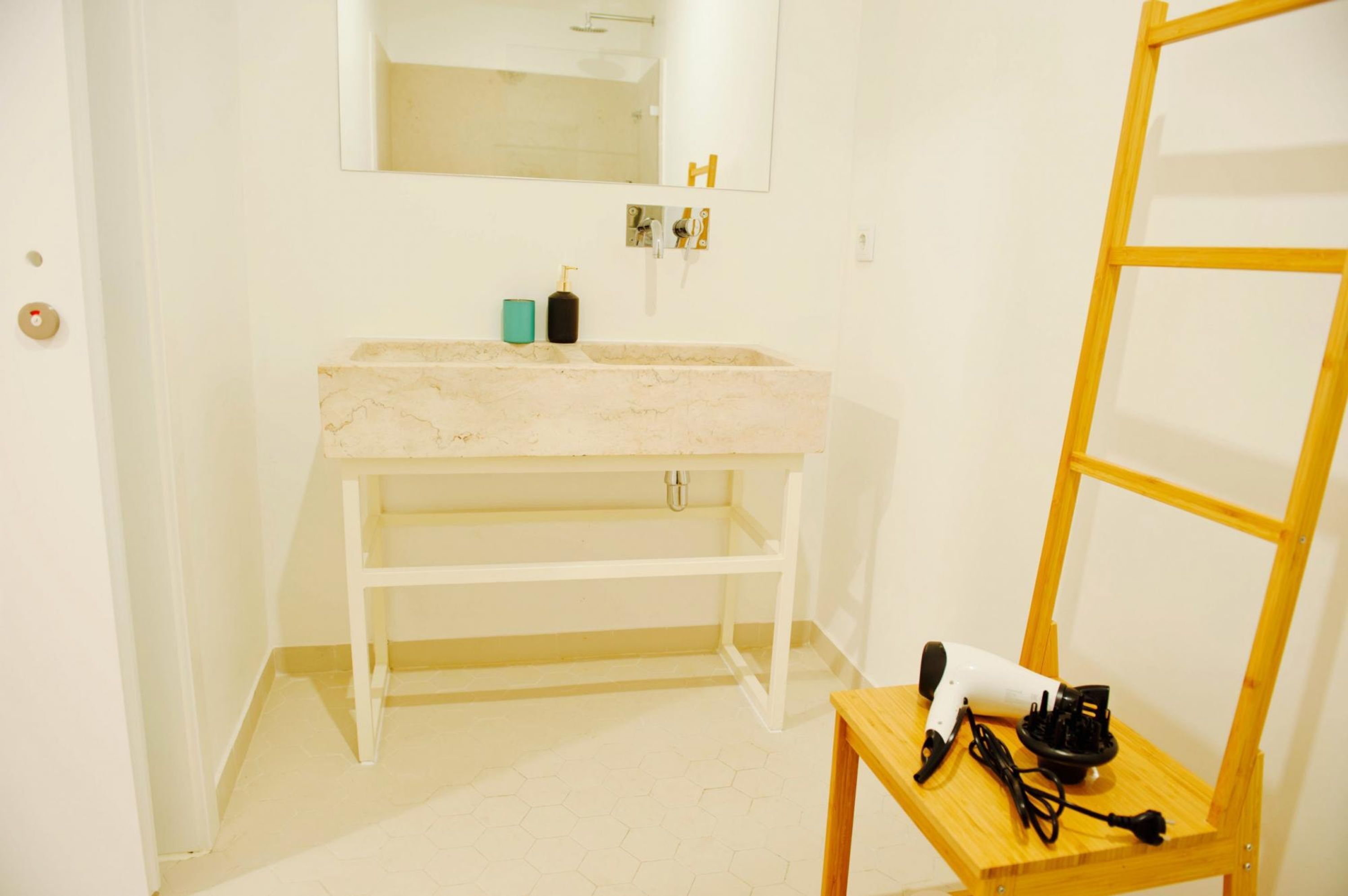 A bathroom with a marble sink, a wooden vanity, a mirror, and a hairdryer on a small table.