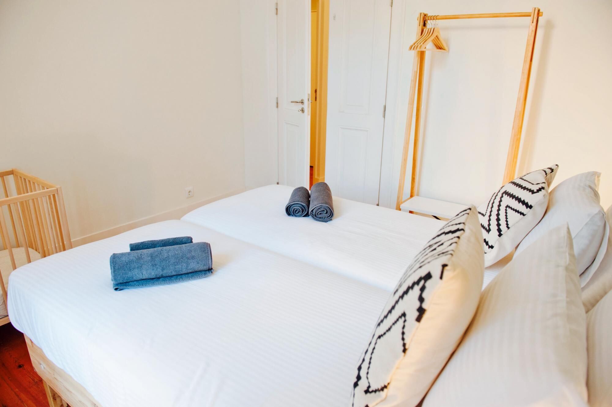 A neatly made bed with white linens, two rolled towels, and patterned pillows.