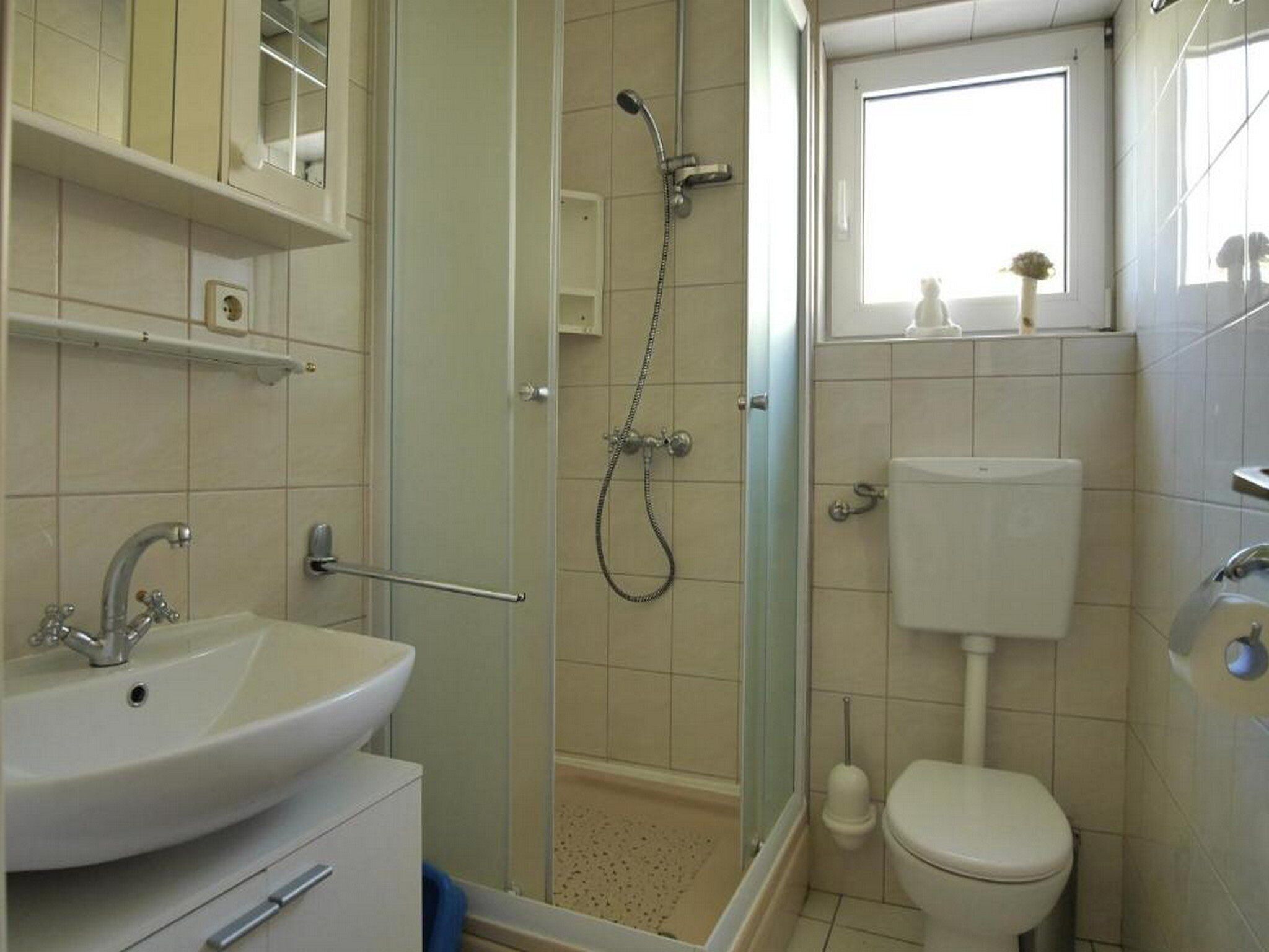 A bathroom with a sink, toilet, shower, and a window.
