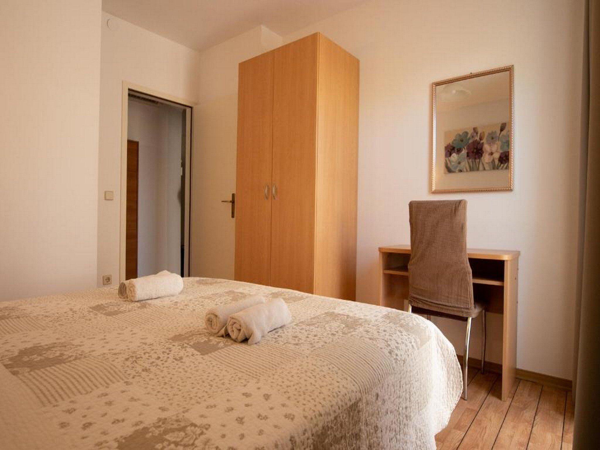 Un dormitorio con cama, armario de madera, escritorio con silla y un cuadro en la pared.
