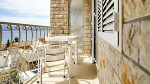 A balcony with a table and chairs, overlooking a body of water and buildings. - Villa Apartments Babaja (Dugi Rat)
