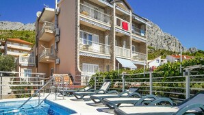 A hotel with a swimming pool, sun loungers, and a mountain backdrop. - Villa Apartments Babaja (Dugi Rat)