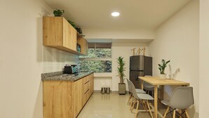 Une cuisine compacte dotée de meubles en bois, d’un plan de travail en granit, d’une cuisinière encastrée, d’un réfrigérateur et d’un coin repas avec une table et des chaises en bois.