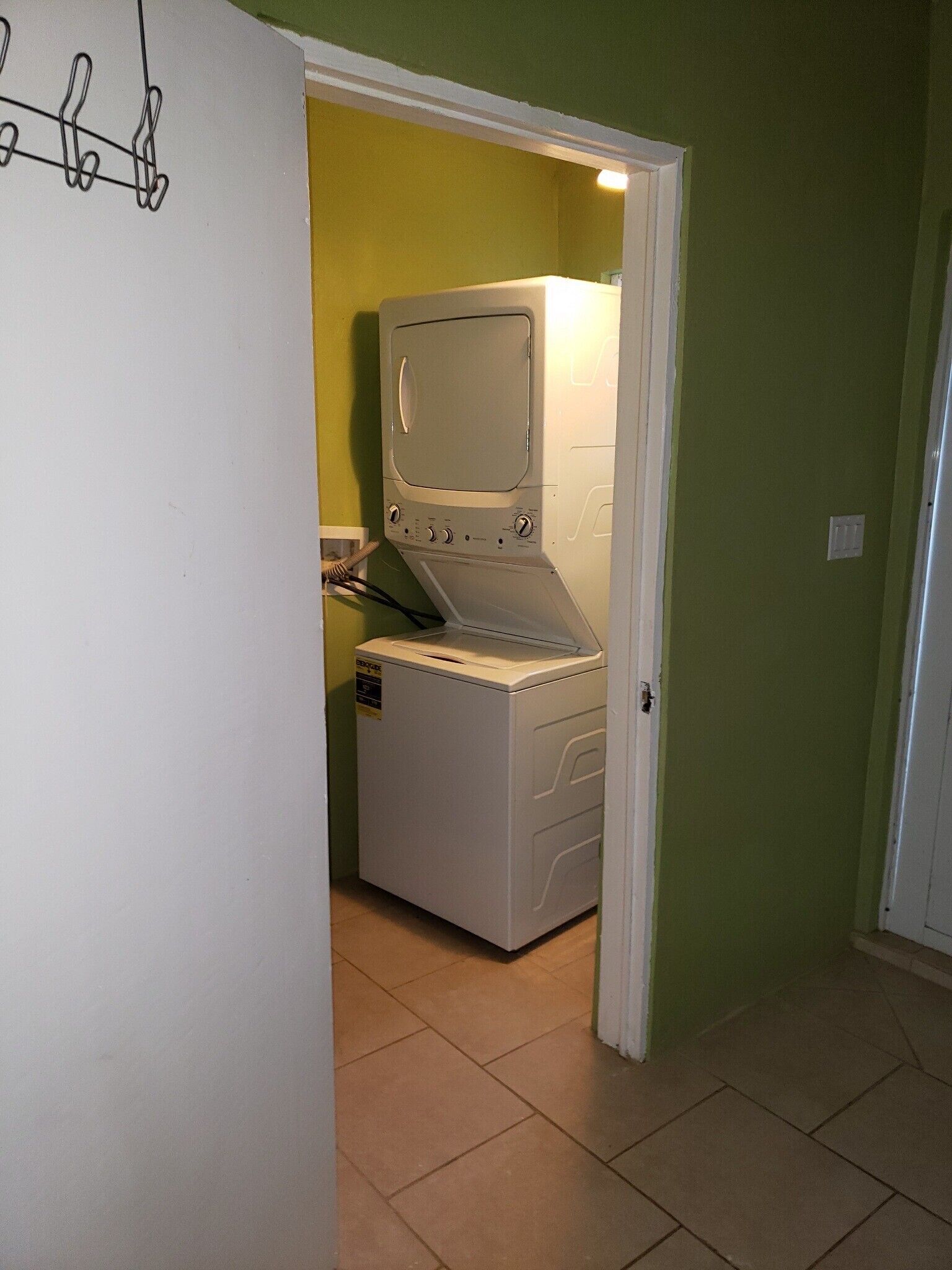 Una sala amb bugaderia, incloent una rentadora i una assecadora, una porta amb penjador de gabardines, i una paret verda.