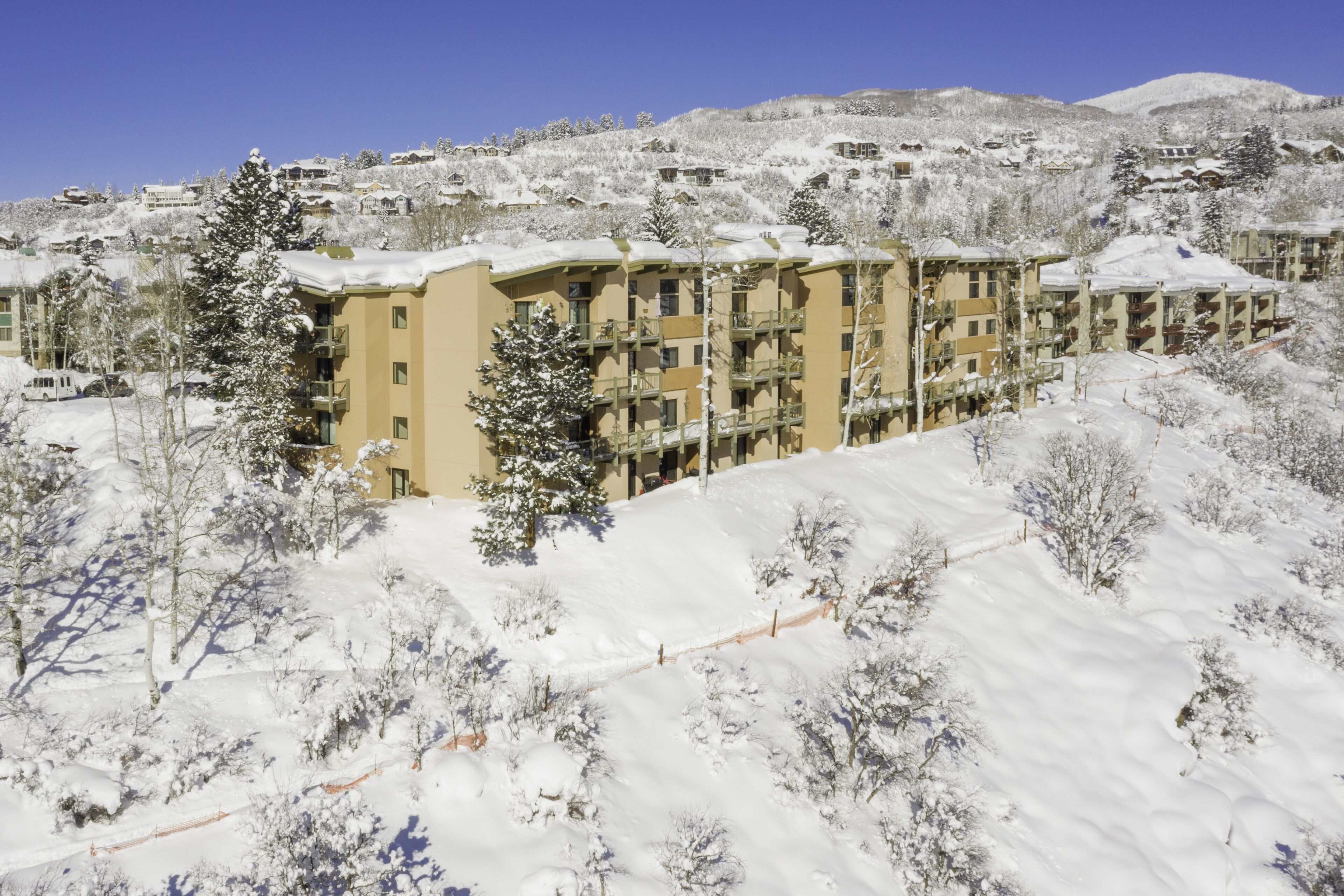 Une colline enneigée, avec un immeuble à plusieurs étages doté de balcons, et une piste de ski au premier plan.