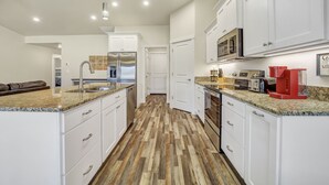 A modern kitchen with white cabinetry, a granite countertop, and a wood-patterned floor. - Comfortable New Home in Broadmoor Subdivision (Twin Falls)