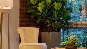A room with a brick wall, a large window with a view of greenery, a white chair, a small round table with a plant, and a floor lamp. - Provenza's Retreat - Tranquil 2BR-2BA Apartment (Medellín)
