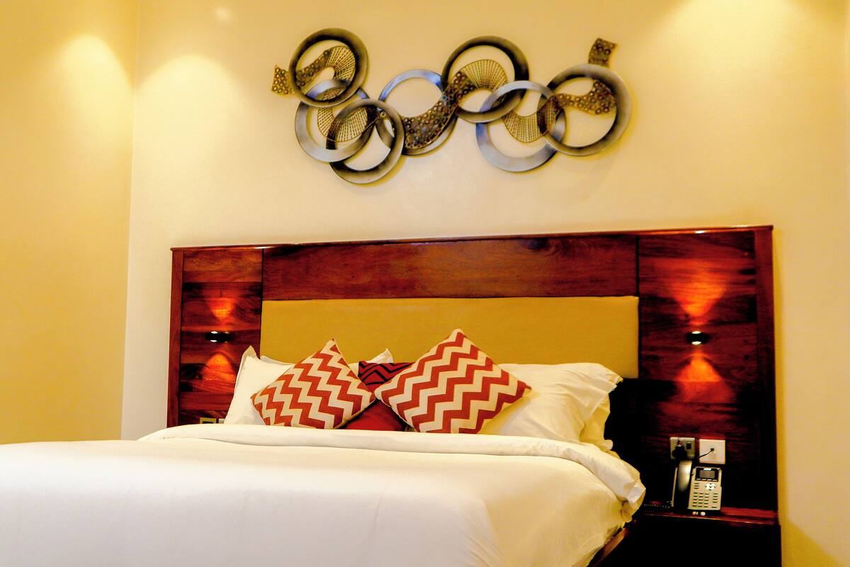 A neatly made bed with white linens and two patterned pillows, a wooden headboard, and a wall-mounted telephone.