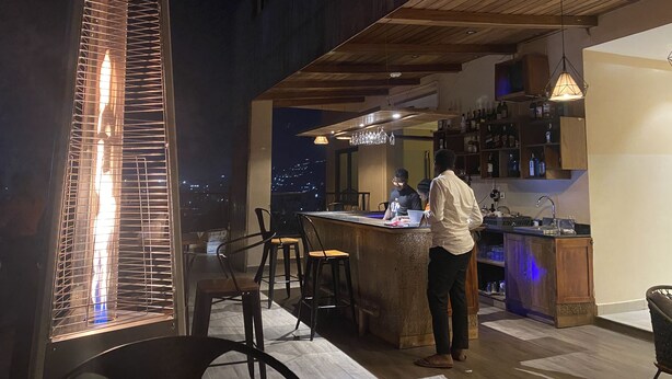 A modern kitchen with a bar area, wooden ceiling, and a view of the city at night. - Millennium Terrace Hotel (Kampala)