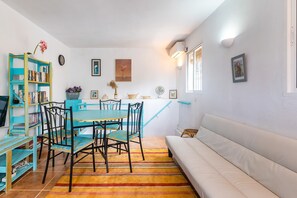 Un coin repas avec une table et des chaises, une bibliothèque, un canapé et une fenêtre avec des stores.