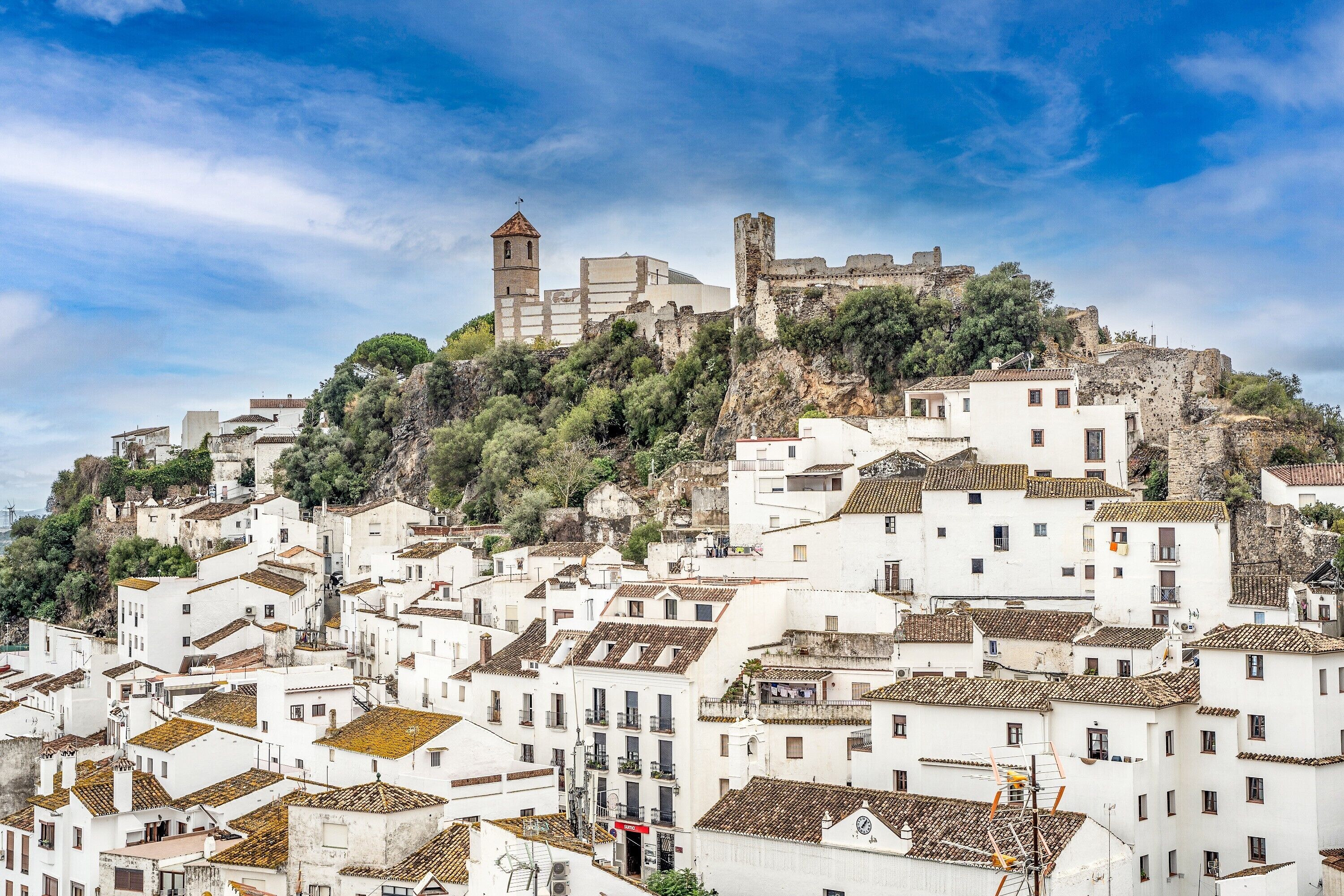 Un pueblo histórico con edificios blancos, una torre de iglesia destacada y un castillo en una colina.